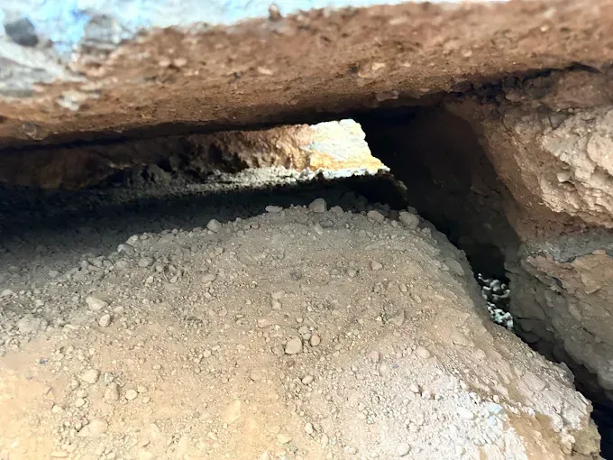 Tunnel-like space between two layers of tan rock and dirt. Sunlight visible at the end of the opening.