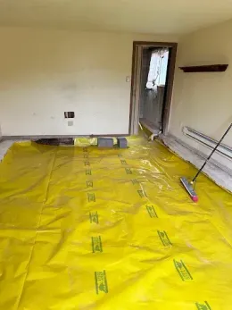 Room with yellow protective covering, door frame, and broom. Walls are cream colored.