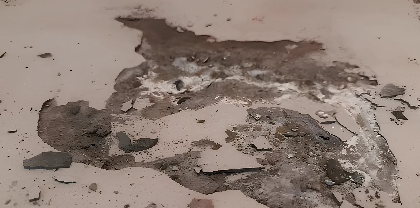Damaged floor with chipped areas, exposing dark concrete and debris against a pale surface.