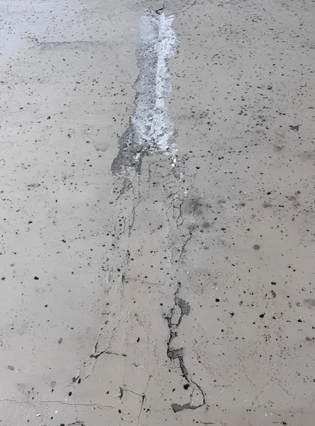 Gray concrete surface with a vertical crack, partially filled with lighter material.