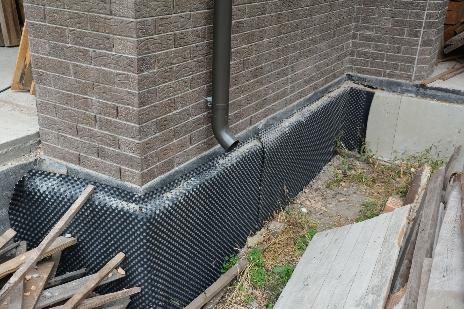 Foundation with black drainage membrane, brick exterior, and a downspout.