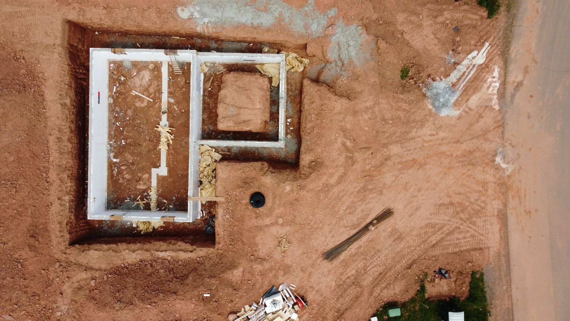 Aerial view of a building foundation outline in red dirt, with concrete walls and a central square.
