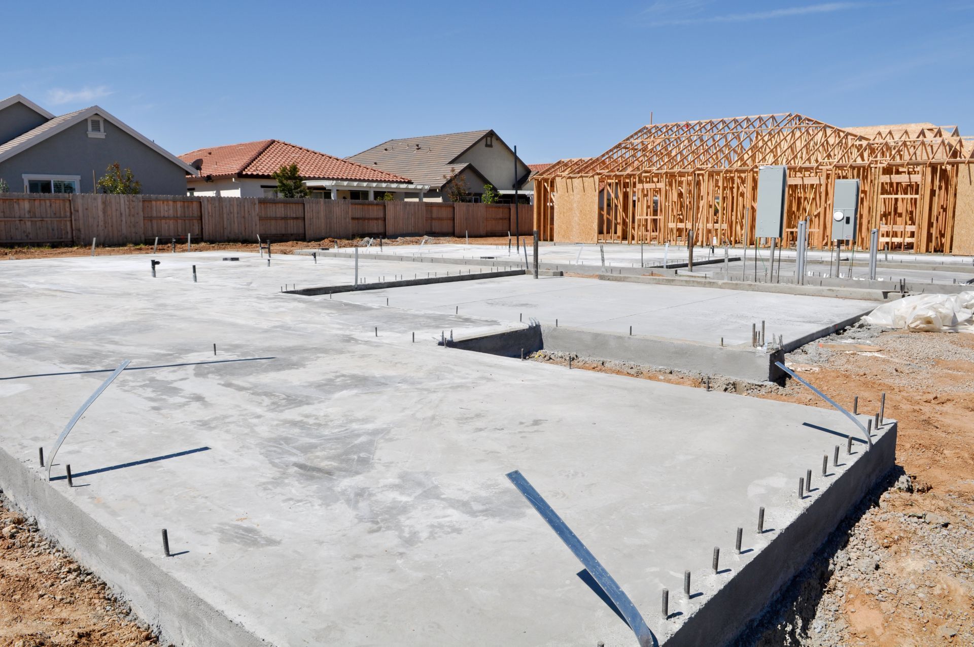 Construction site with concrete foundation and framed house, blue sky background.