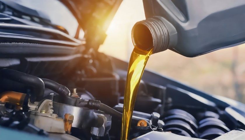 Golden motor oil pours from a plastic container into a car engine during an oil change.