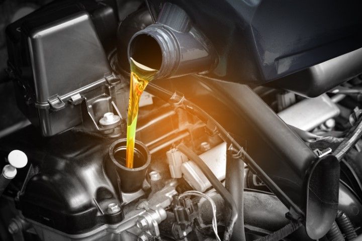 Golden motor oil is being poured from a plastic container into a car engine's oil fill port.