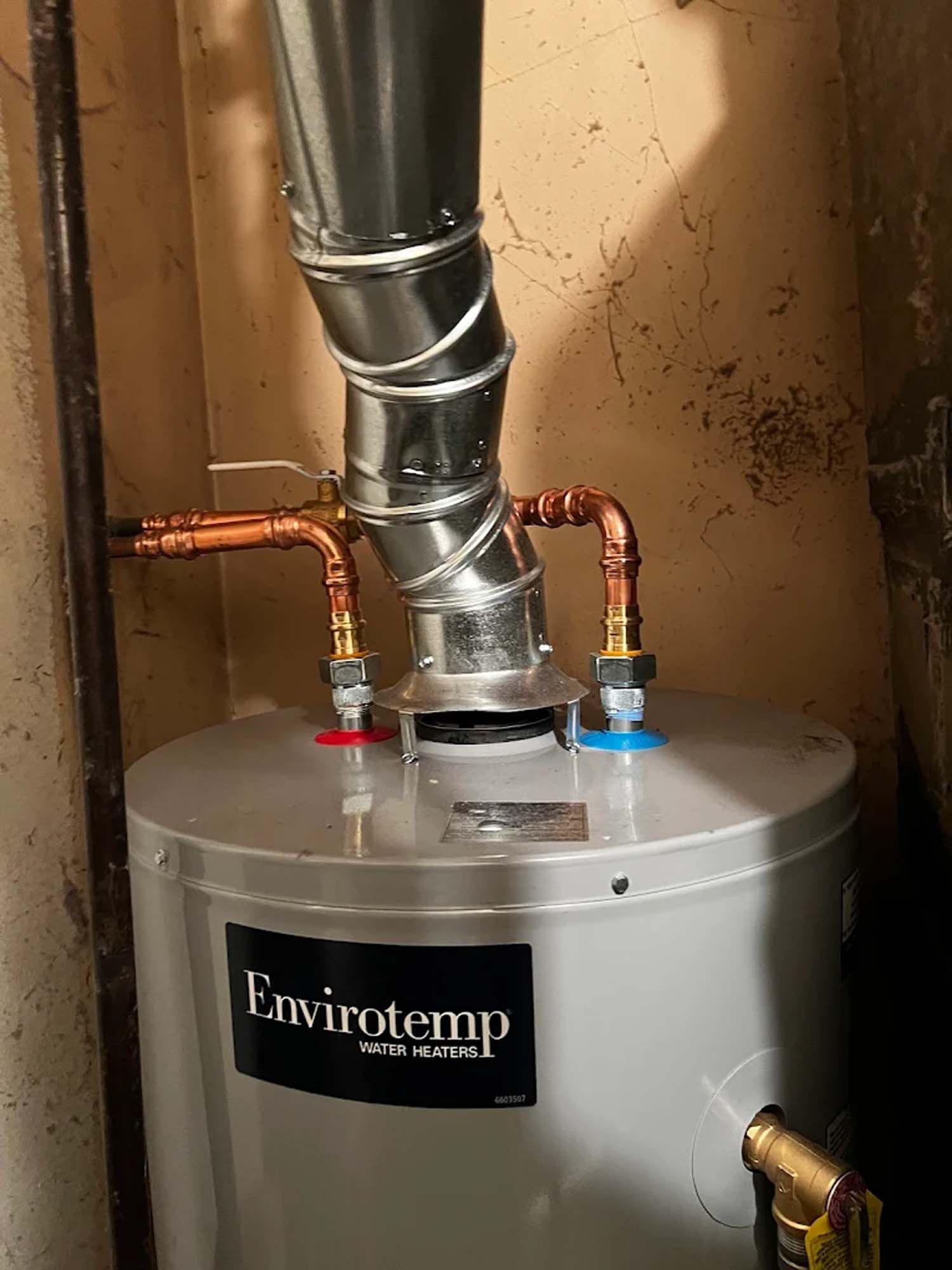 Water heater with copper pipes and vent, indoors.