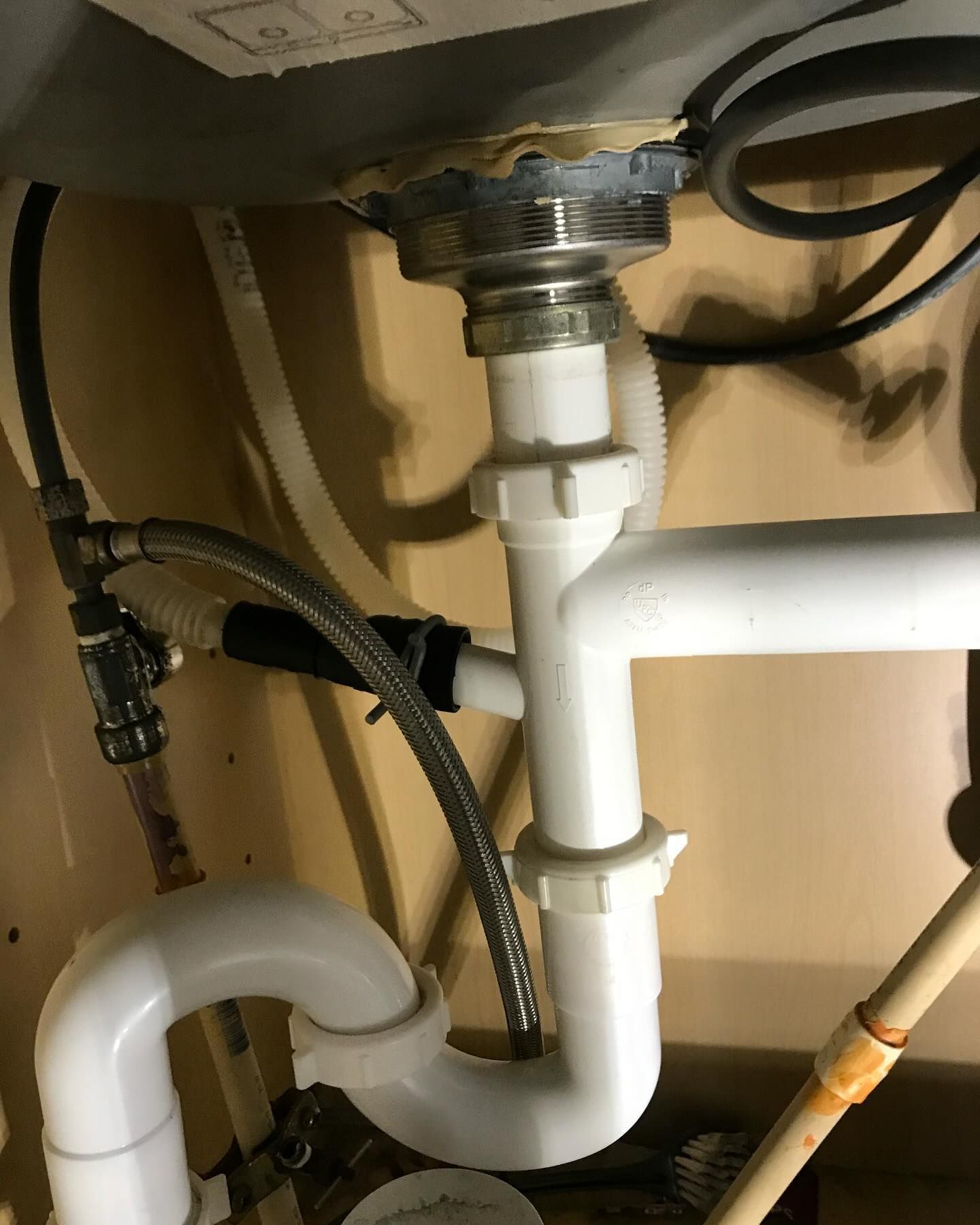 Under-sink plumbing, mostly white plastic pipes, connecting to a chrome drain above and a copper pipe with faucet connector on the left.