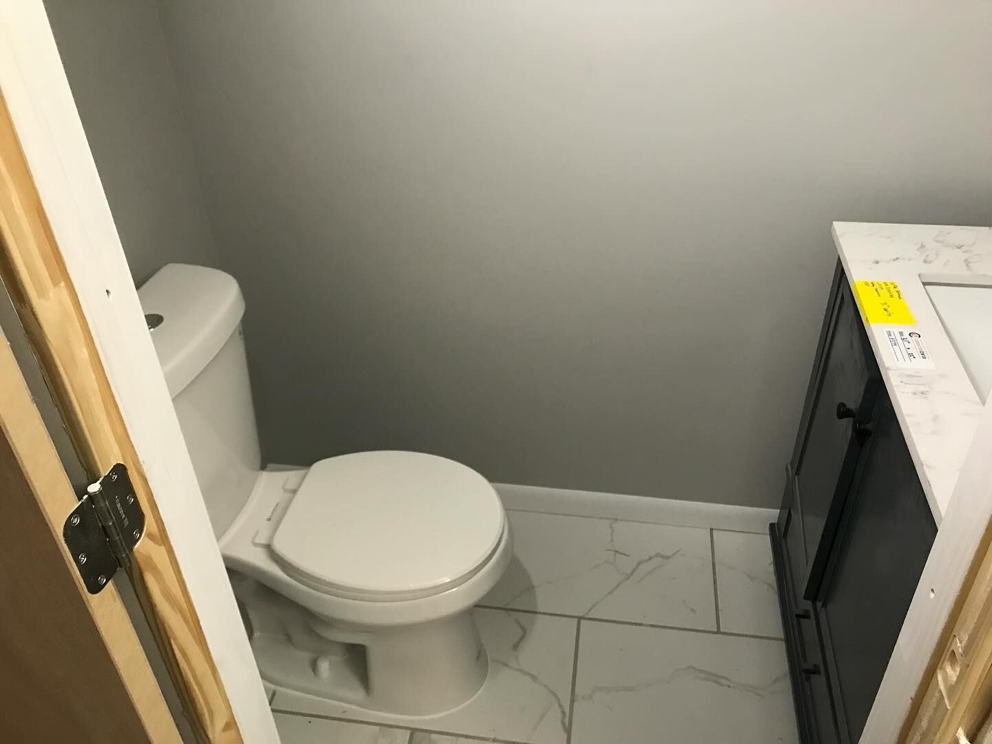 A small bathroom with a toilet, vanity, and gray walls. The floor has white tile.