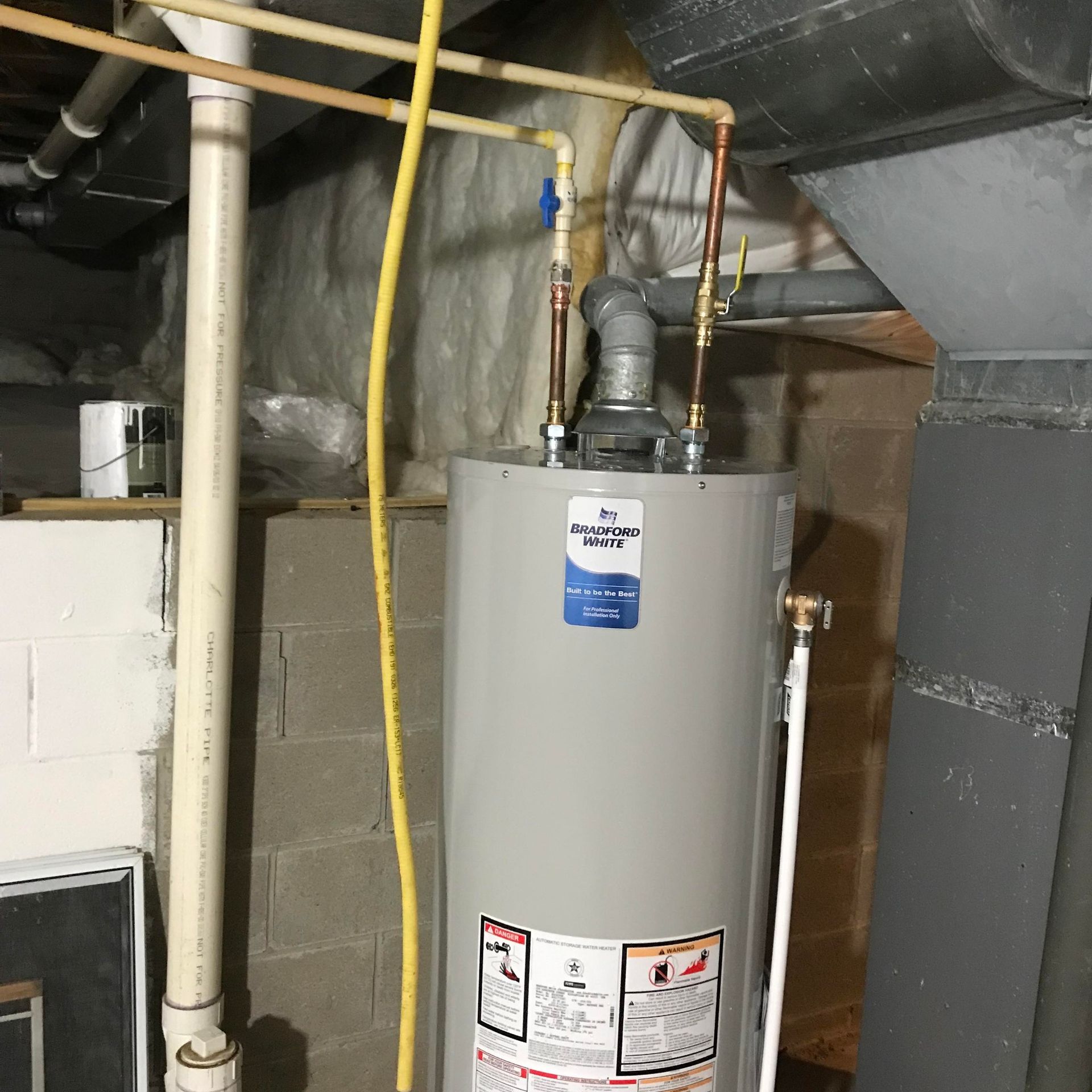 A water heater in a basement with white pipes, a yellow gas line, and a gray flue.