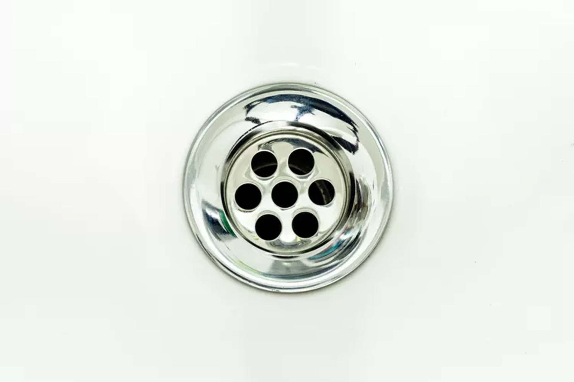Shiny, chrome sink drain with seven holes, in a white sink.