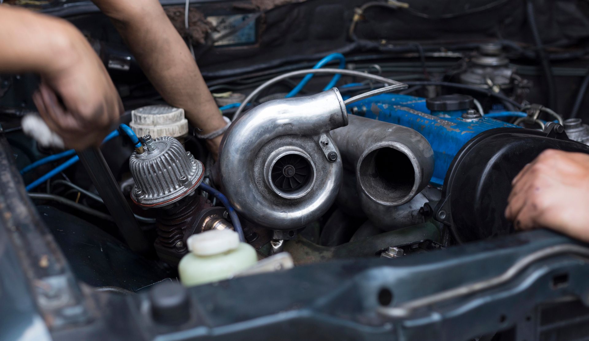 Mani al lavoro su un motore d'auto con tubi del turbo lucidi e cavi blu nel vano motore.