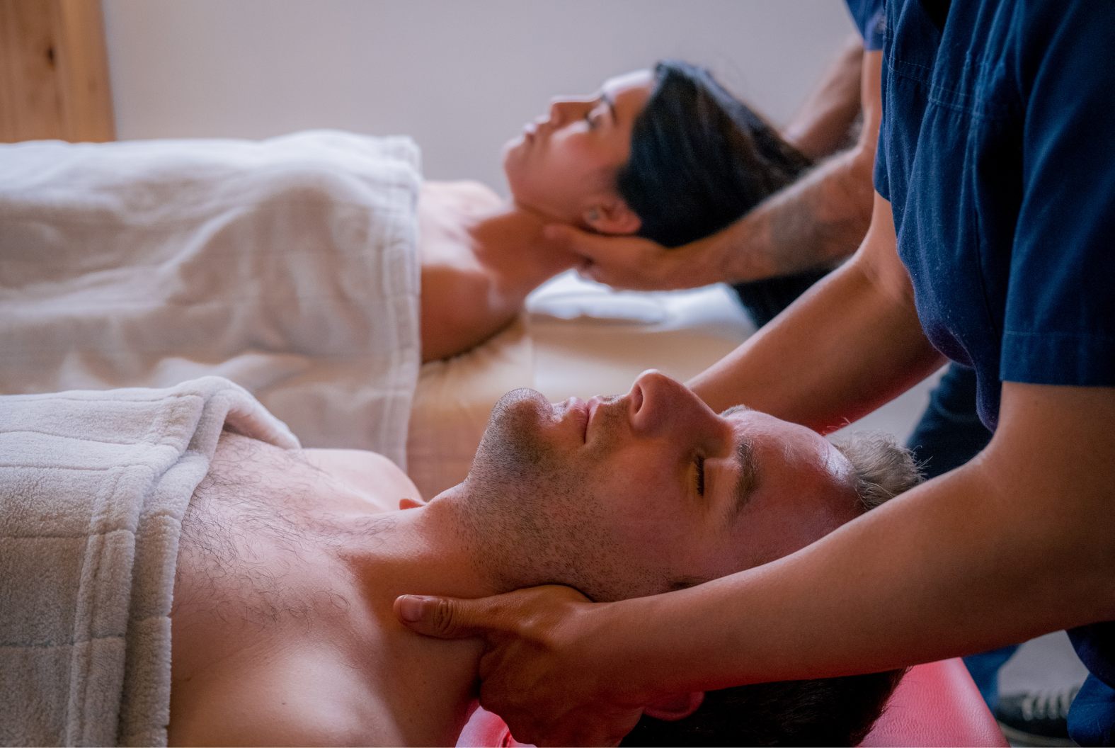 Two people receiving neck massages in a spa-like setting. Therapists' hands on necks.