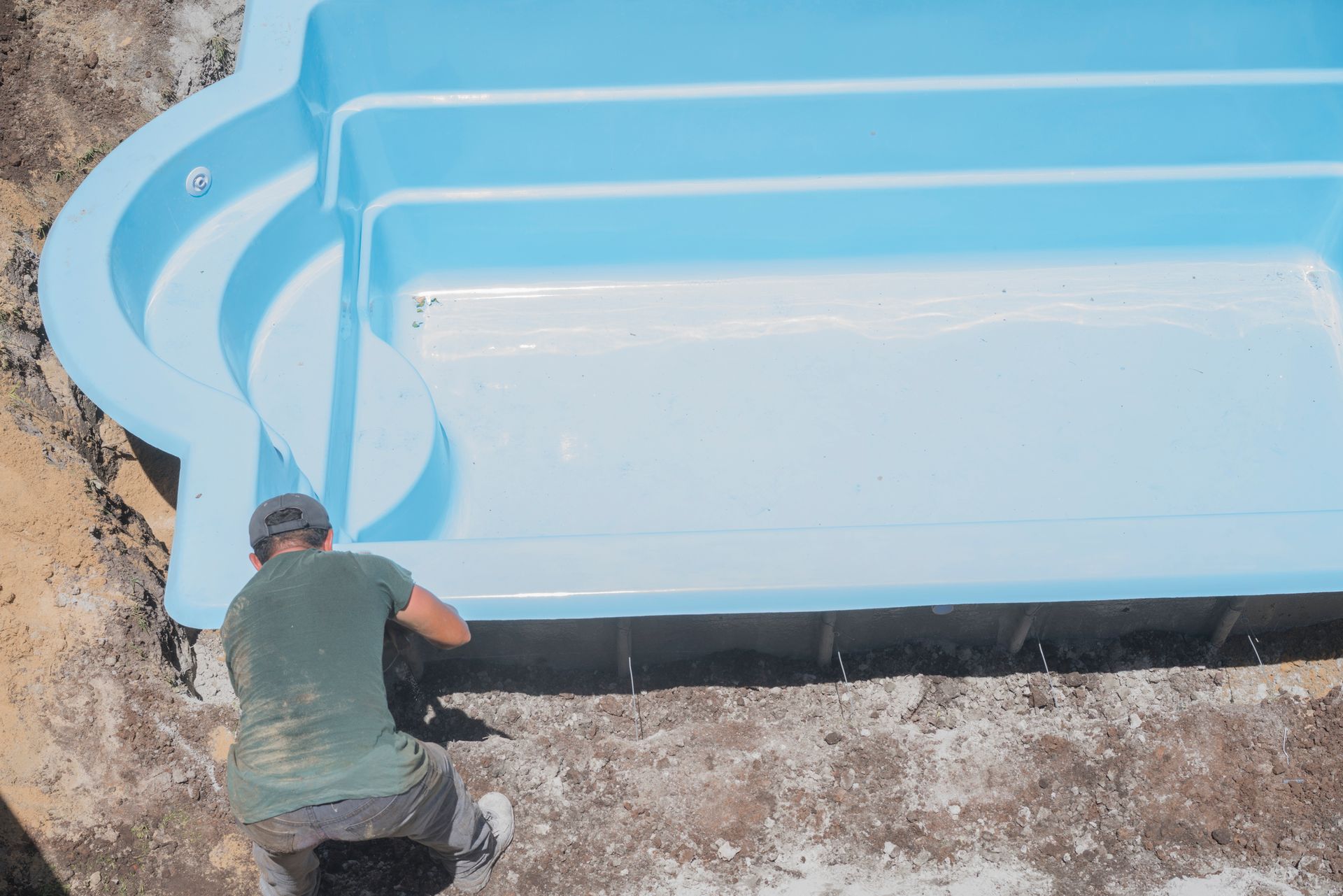 Construction workers are installing a swimming pool at a house backyard on a sunny day. Construction workers are installing a swimming pool at a house backyard on a sunny day.