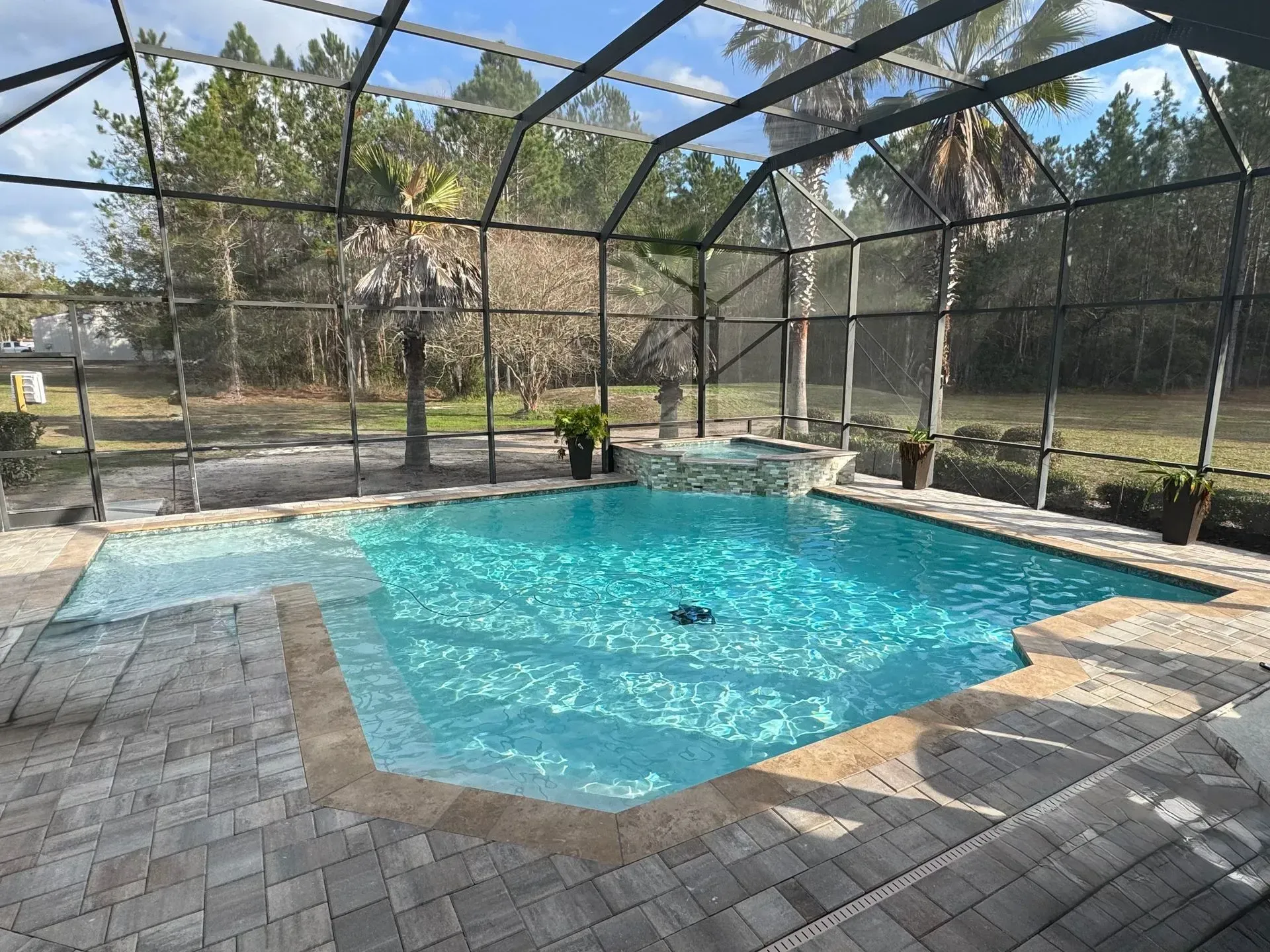Screened-in backyard pool with blue water, paver deck, and trees beyond the enclosure