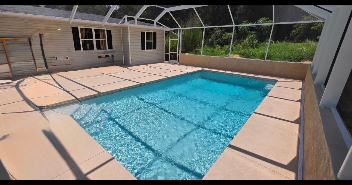 Rectangular backyard swimming pool with turquoise water and beige pool deck beside a screened patio