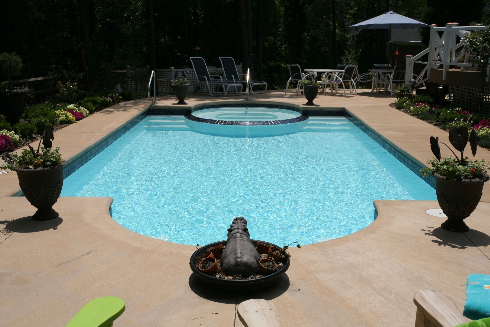Sunny backyard pool with a circular spa, lounge chairs, potted flowers, and umbrellas