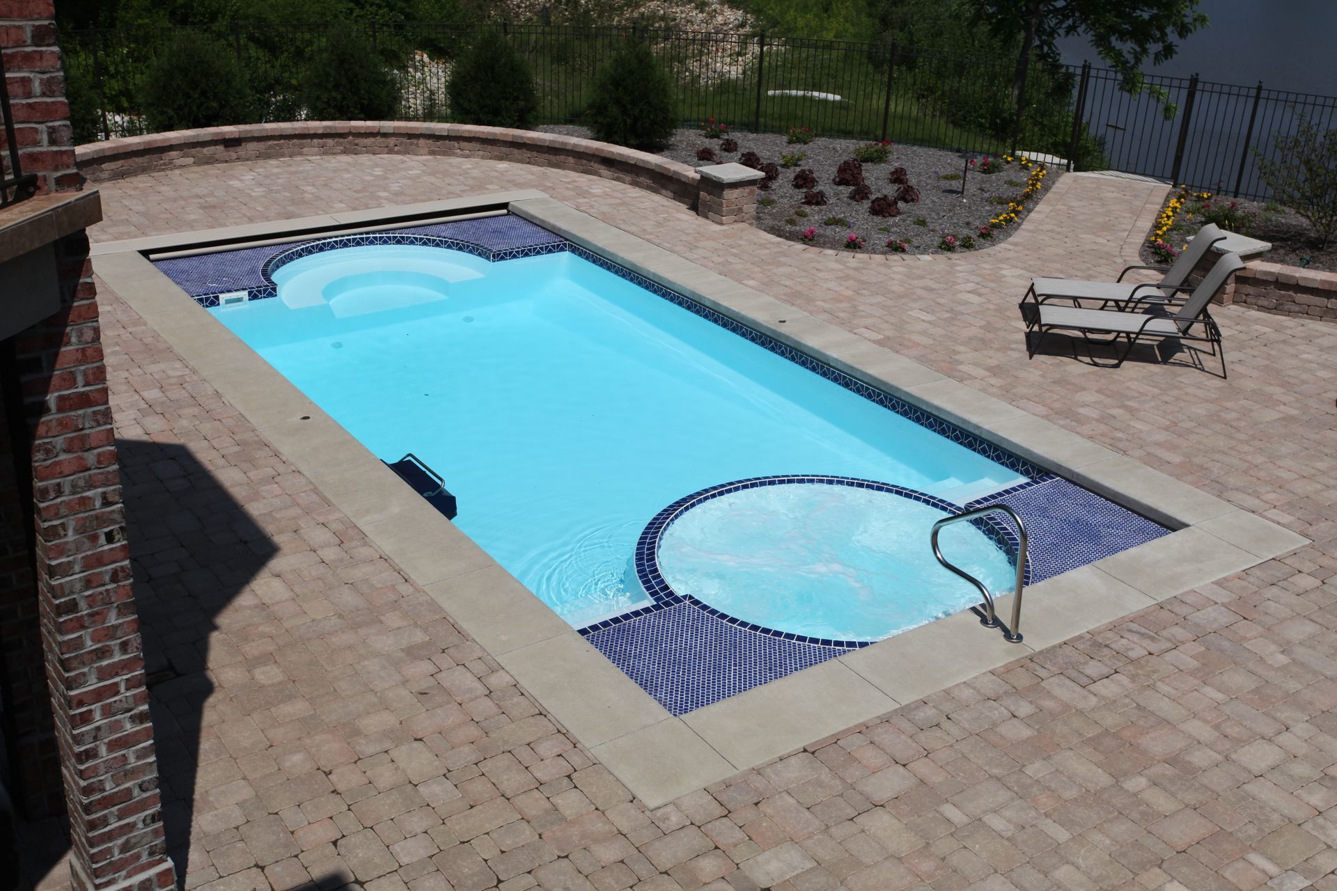 Backyard swimming pool with built-in hot tub and a lounge chair on a stone patio