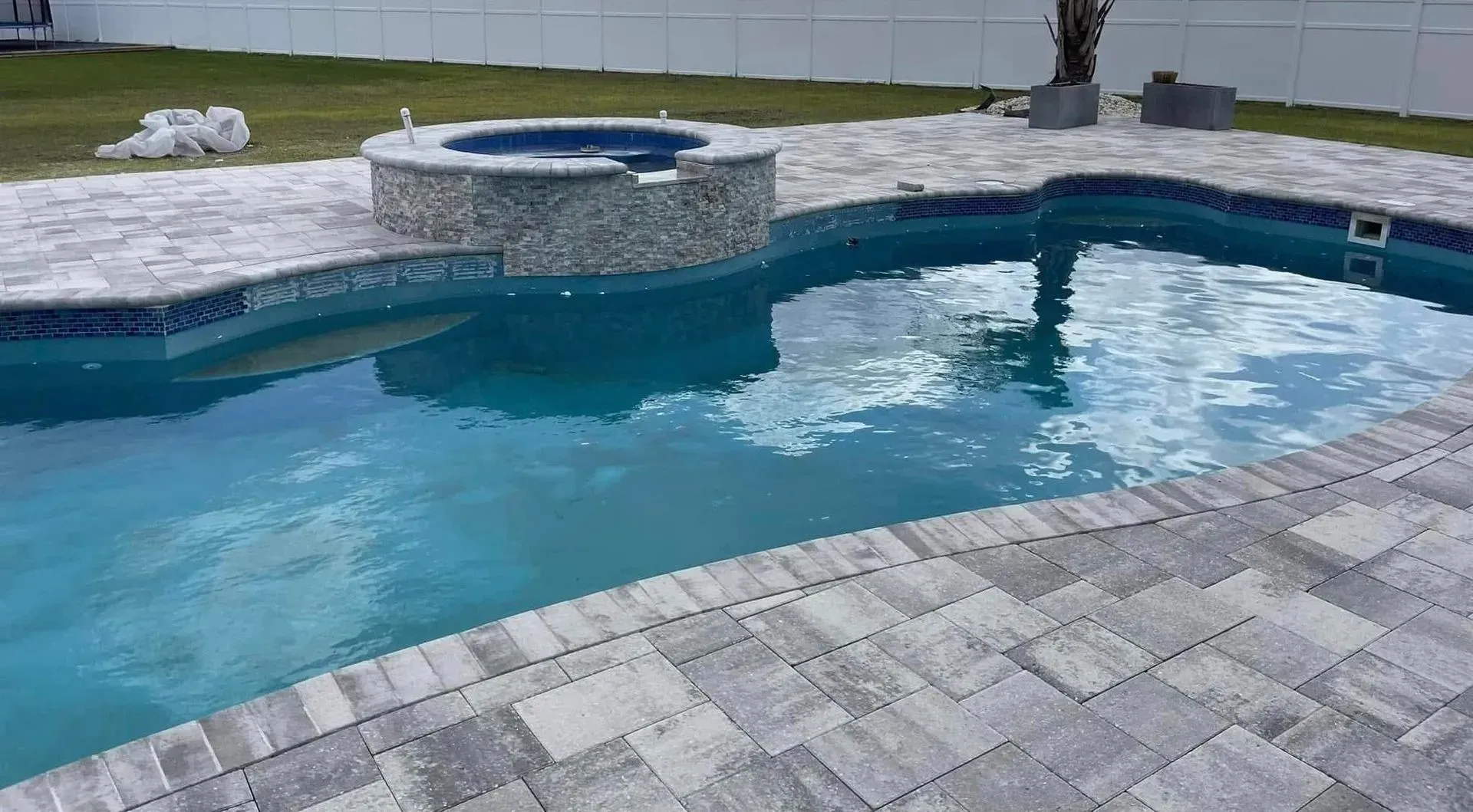 Backyard pool with blue water, stone coping, and a raised spa on a paved patio.