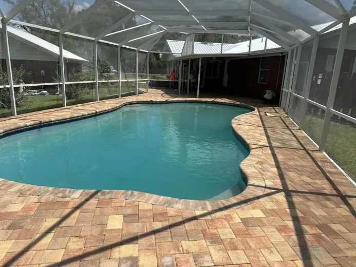 Screened-in backyard pool with turquoise water and brick deck in bright sunlight