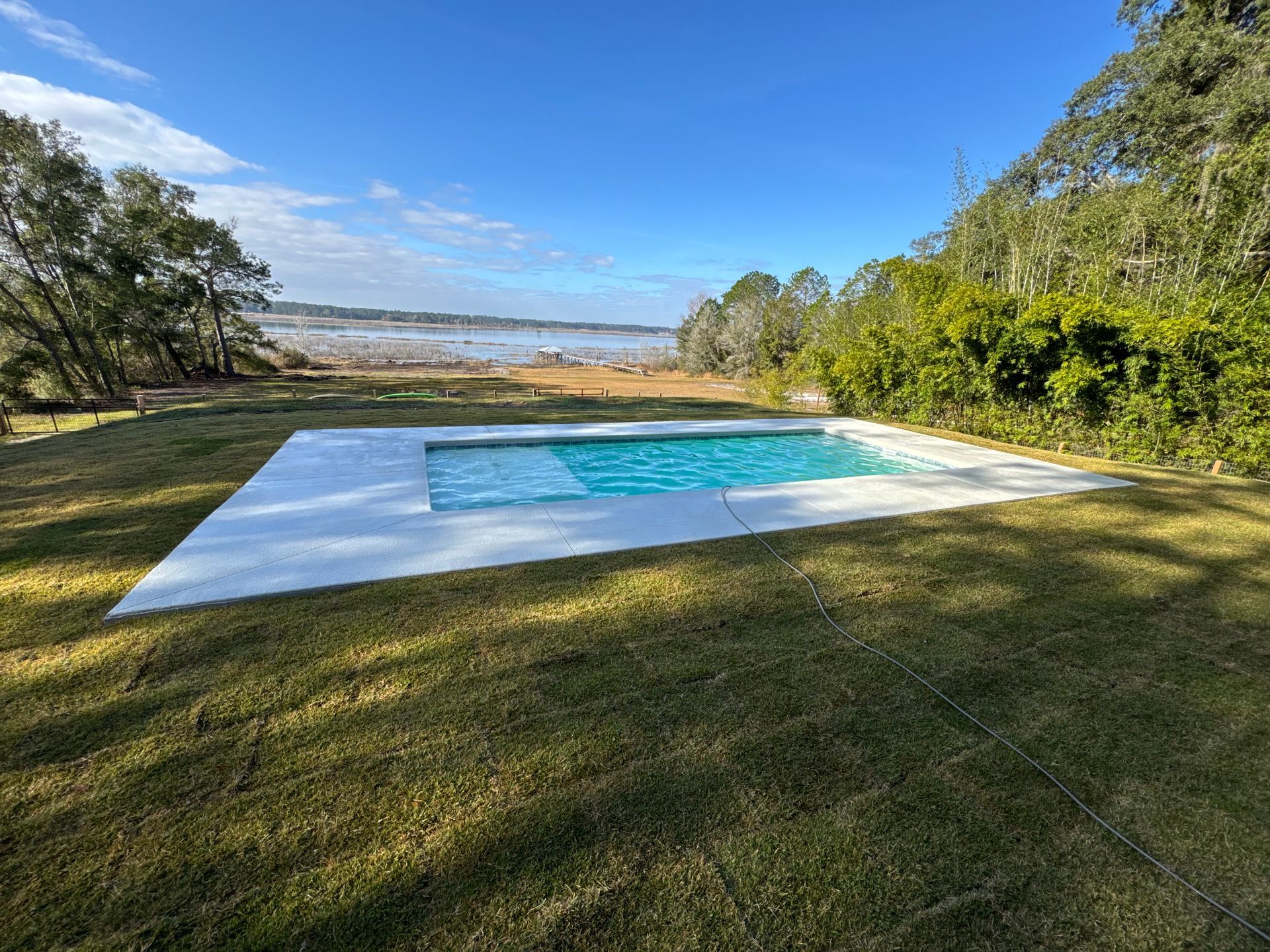 Poolside patio with pergola and screened enclosure. Brown pergola, blue pool, stone patio.