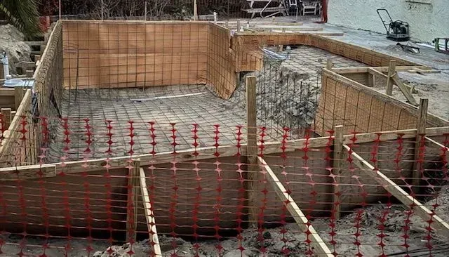Concrete foundation construction site with rebar, wooden forms, and orange safety netting