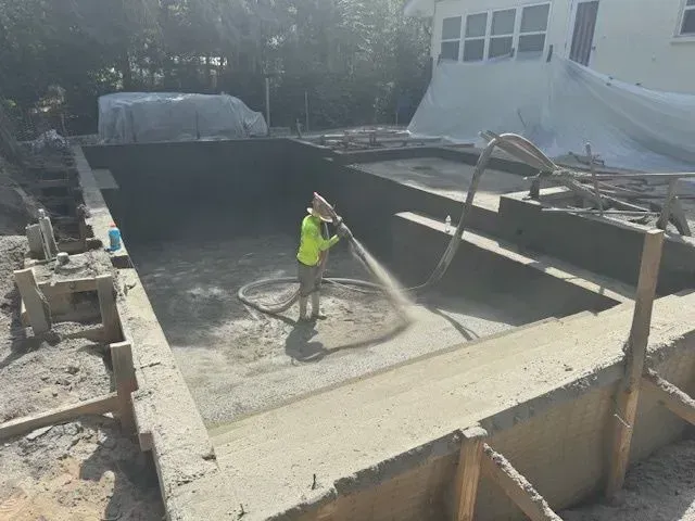 Worker spraying concrete inside a large rectangular pool under construction