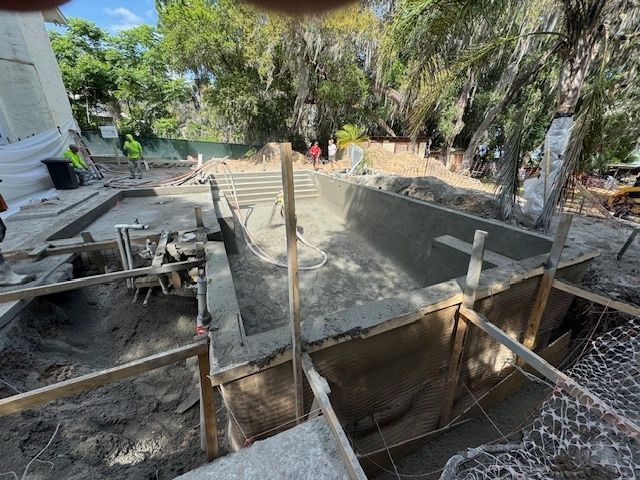 A concrete pool is being built in a yard with trees in the background.