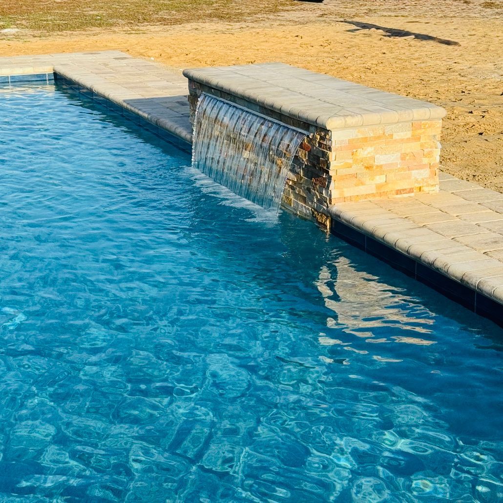 Man in cap and shirt smiles, stands in dirty pool holding rope, red bucket at feet.