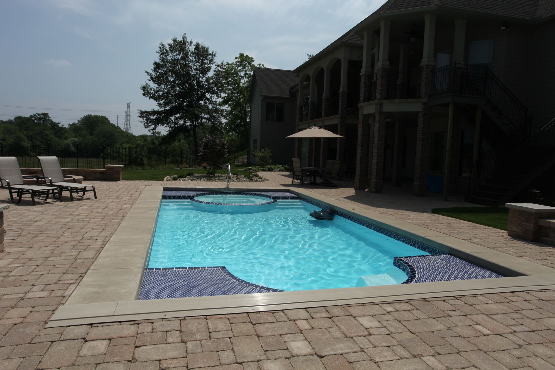 Backyard pool with blue water, lounge chairs, and a house patio on a sunny day