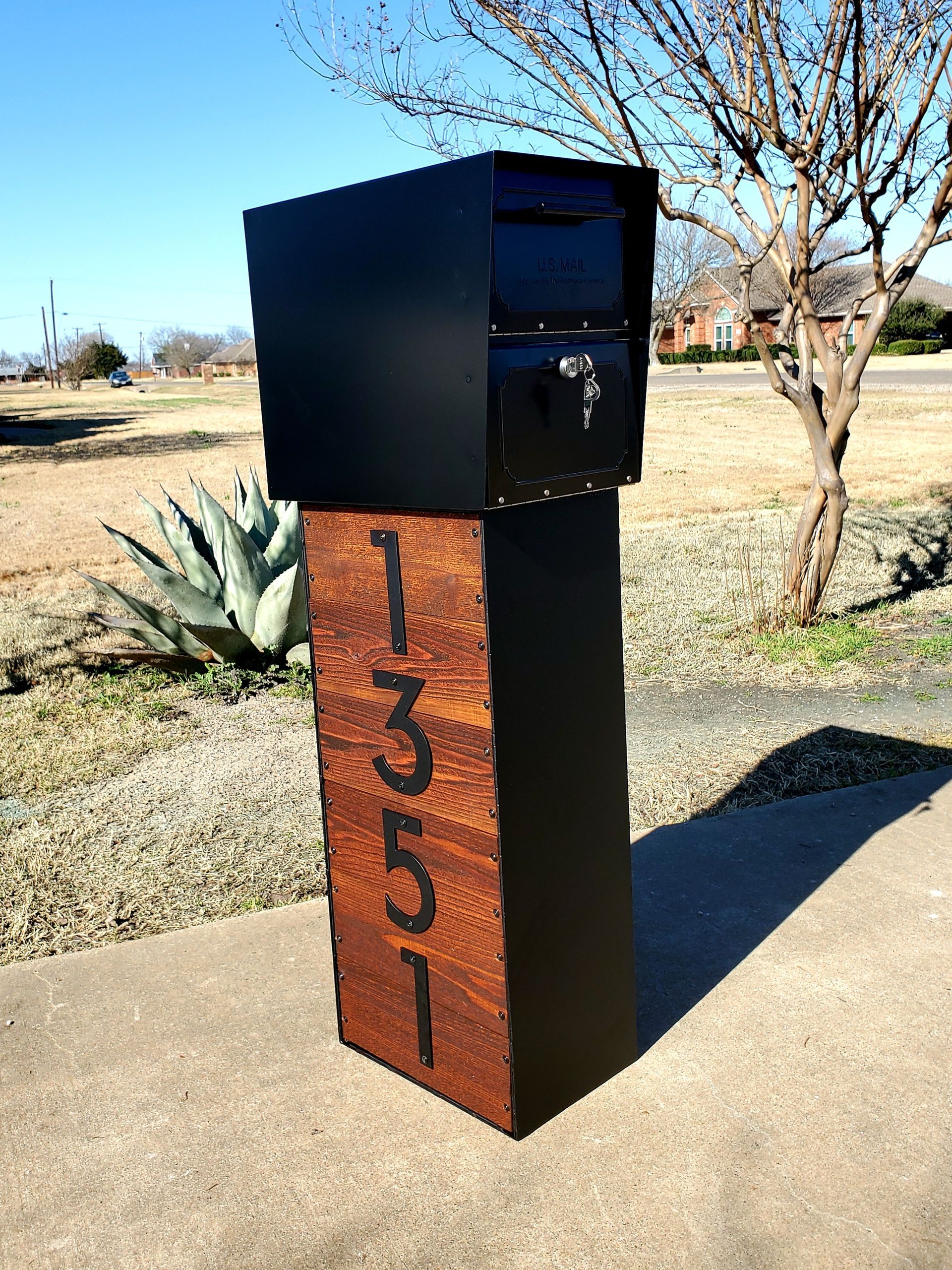 A mailbox is sitting on a sidewalk next to a tree.