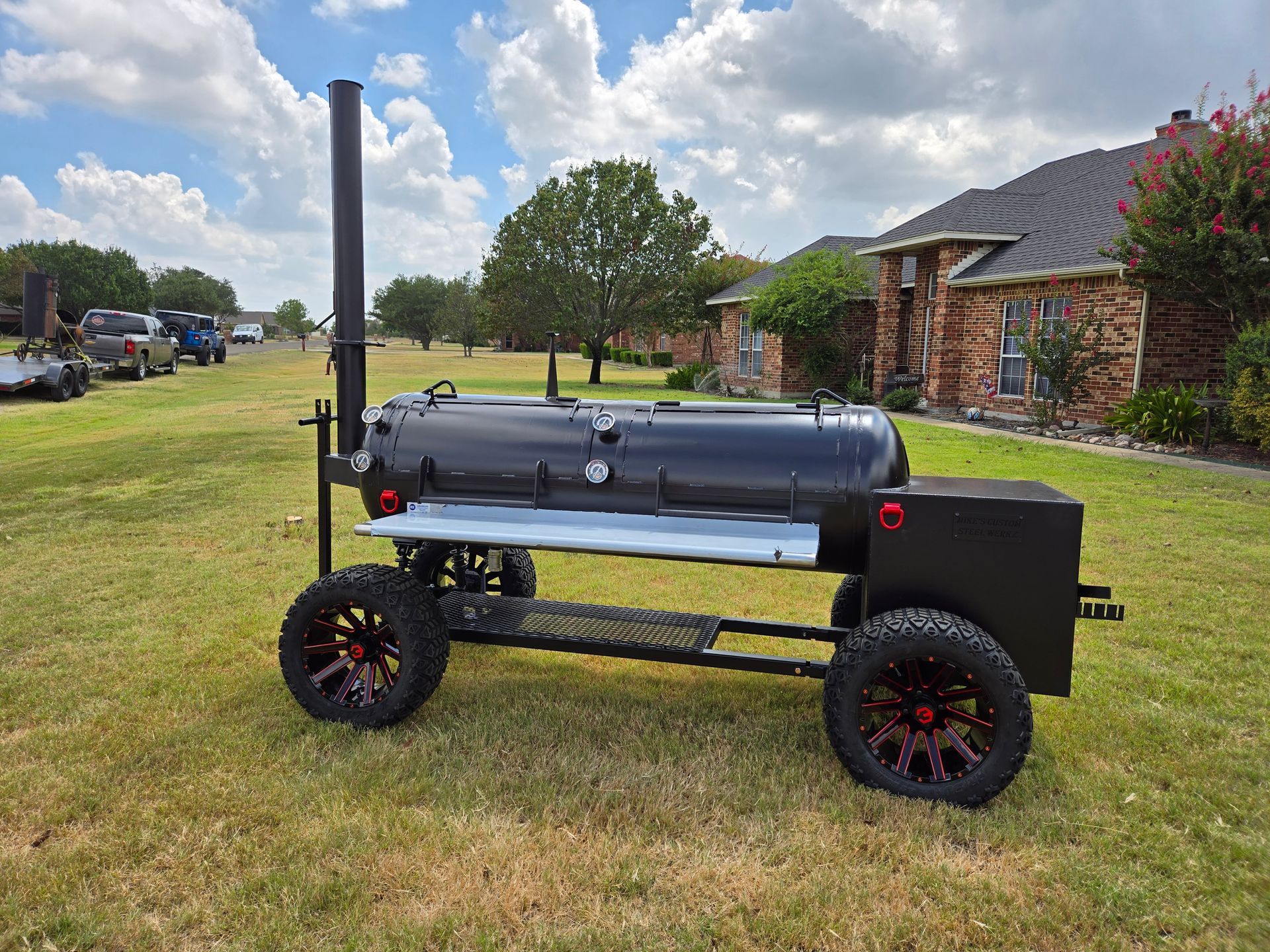 A large bbq grill on wheels is parked in a grassy field in front of a house.