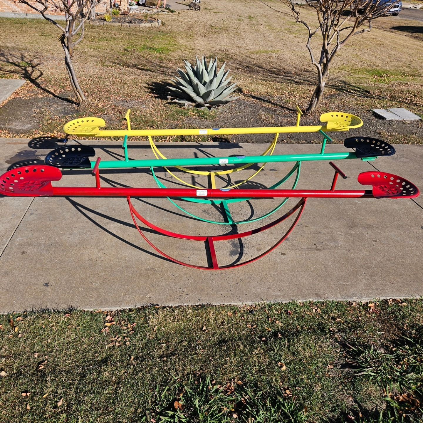 A colorful seesaw is sitting on a sidewalk in a park.