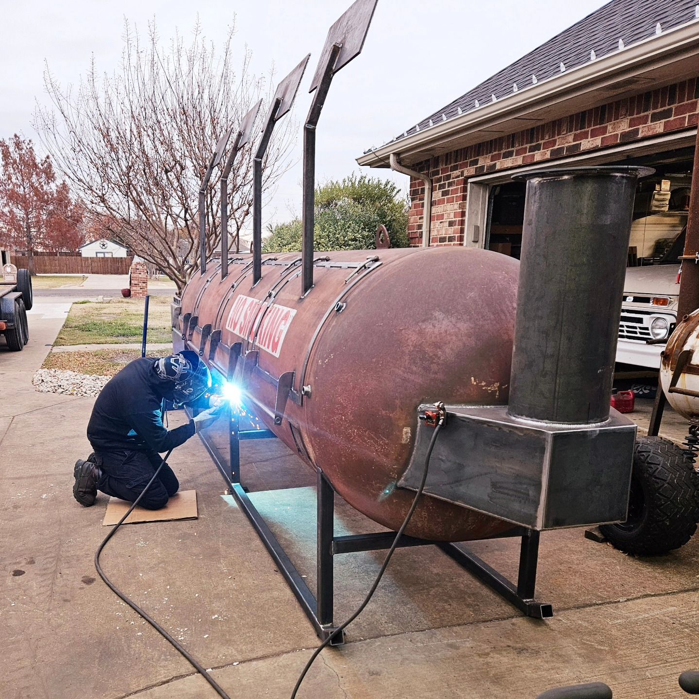 A man is welding a large metal object in front of a house