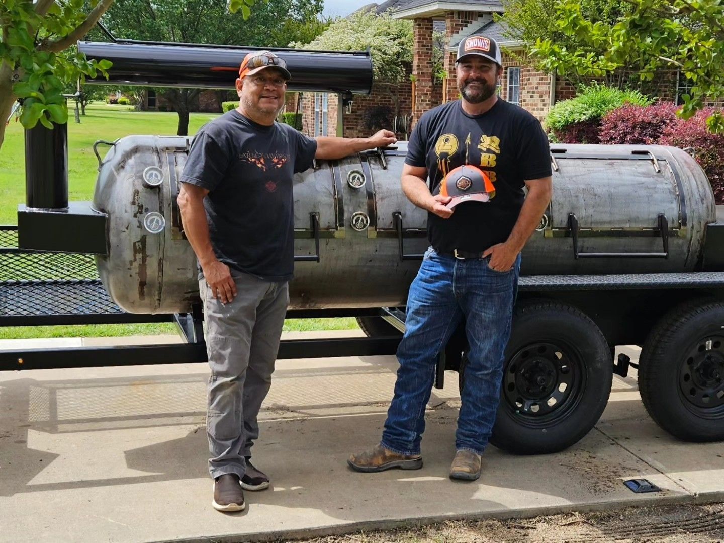Two men are standing next to each other in front of a grill.