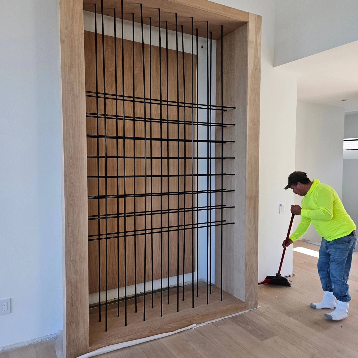 A man in a neon yellow shirt is sweeping a room with a broom.
