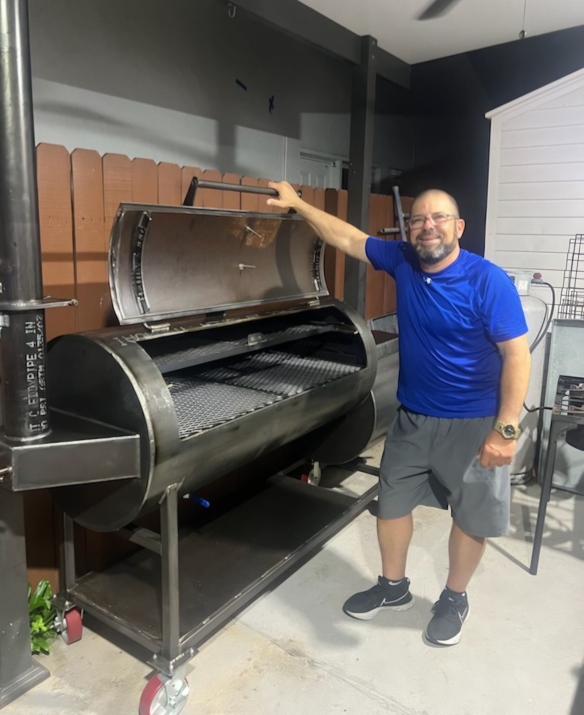 A man in a blue shirt is standing in front of a large grill.