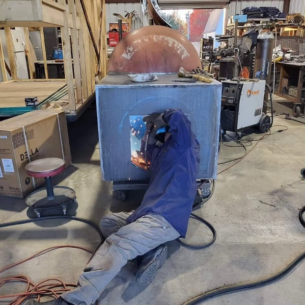 A man wearing a welding mask is working on a piece of metal