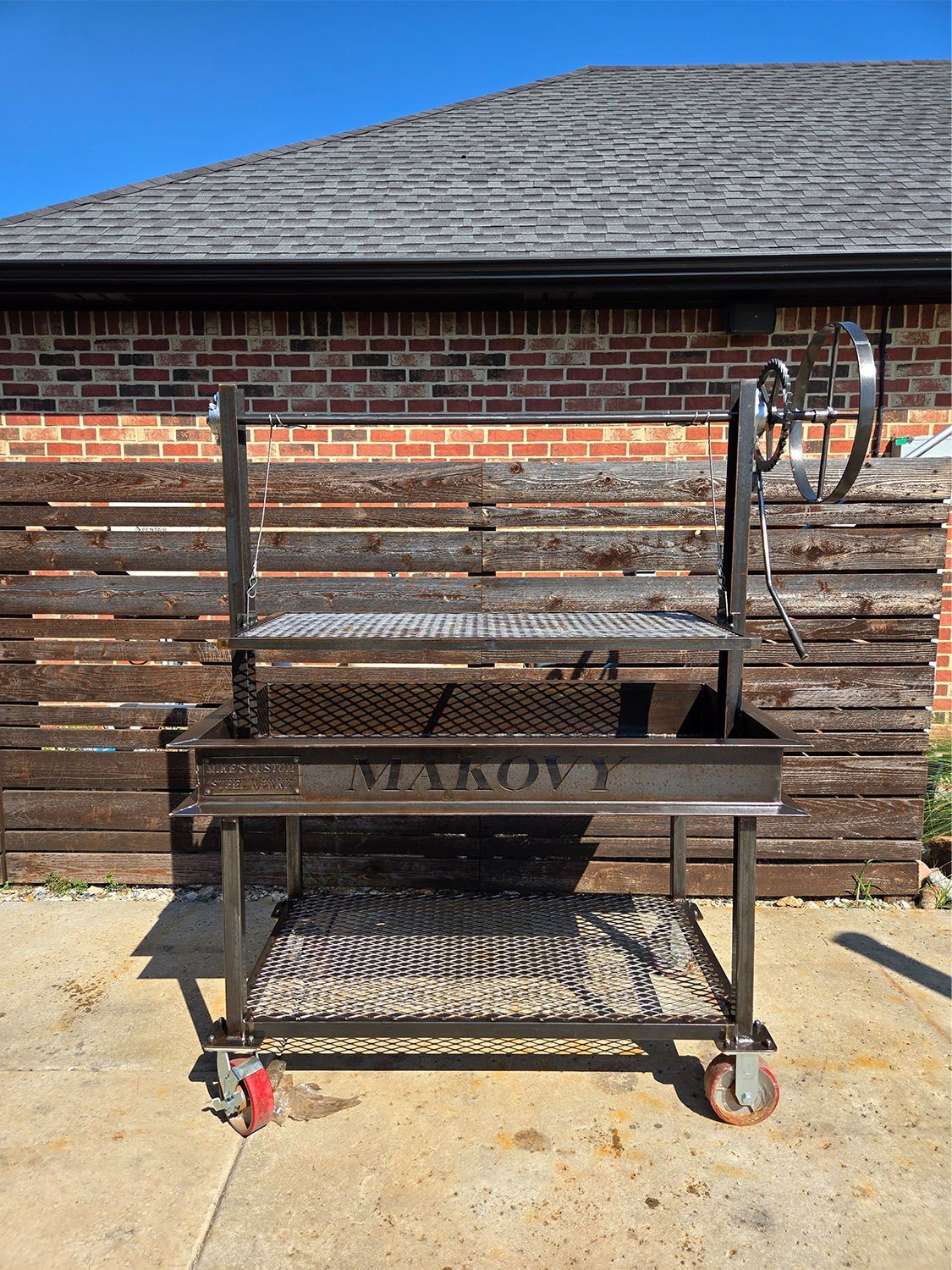A large bbq grill on wheels is parked in a grassy field in front of a house.