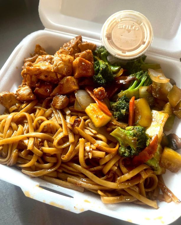 A styrofoam container filled with noodles , meat and vegetables.