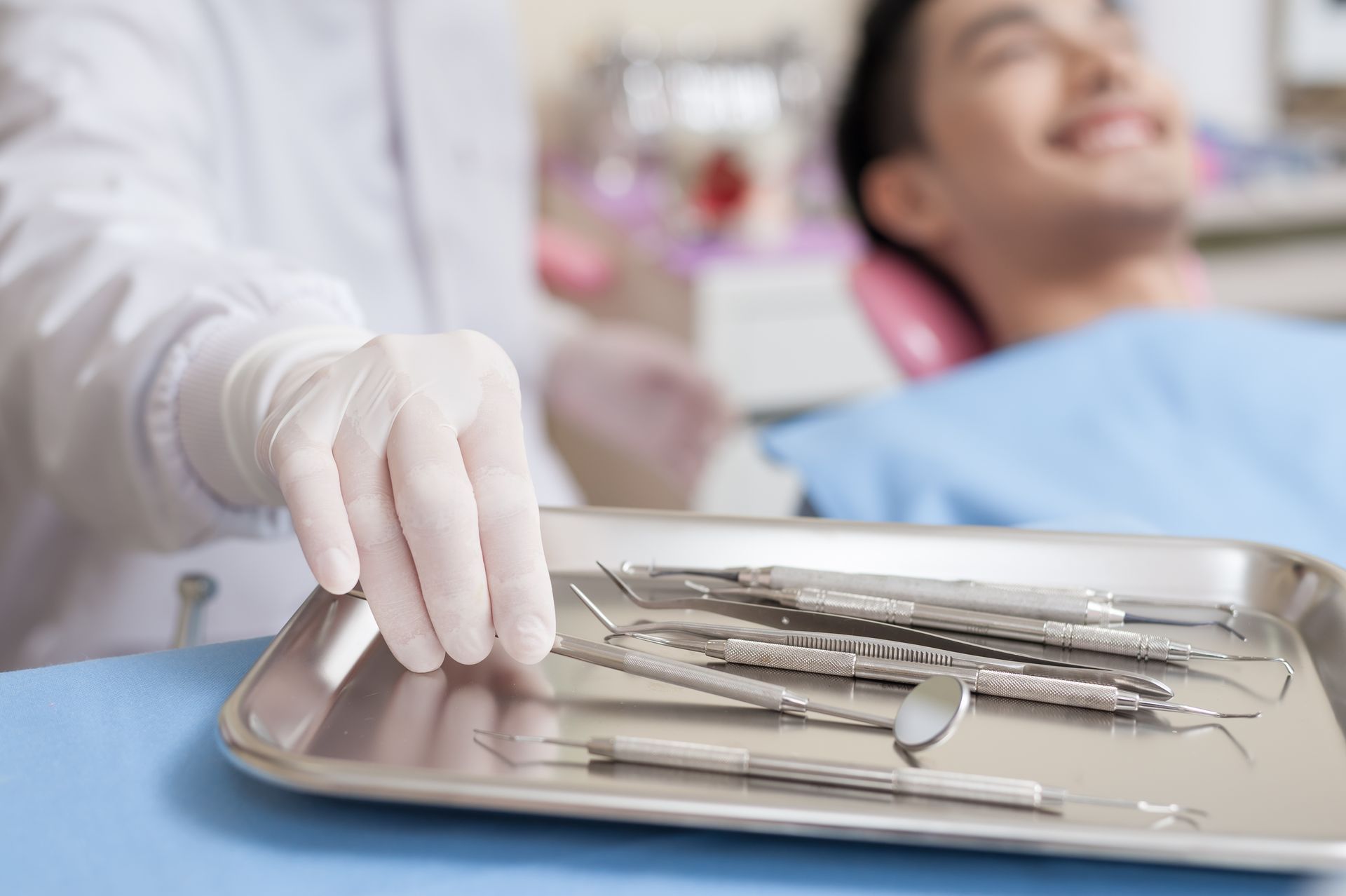 Dentist reaching for dental instruments on a tray during a patient visit.