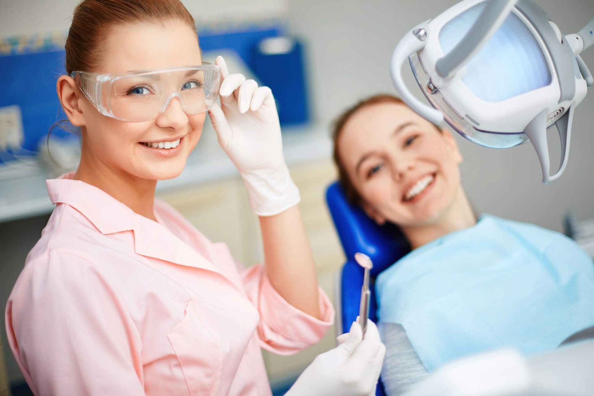 Dentist in uniform looking at camera with her patient on background Dentist in uniform looking at camera with her patient on background