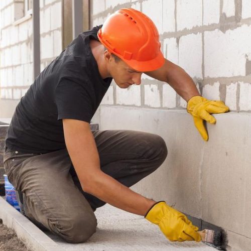 A man wearing an orange hard hat and yellow gloves is working on a wall