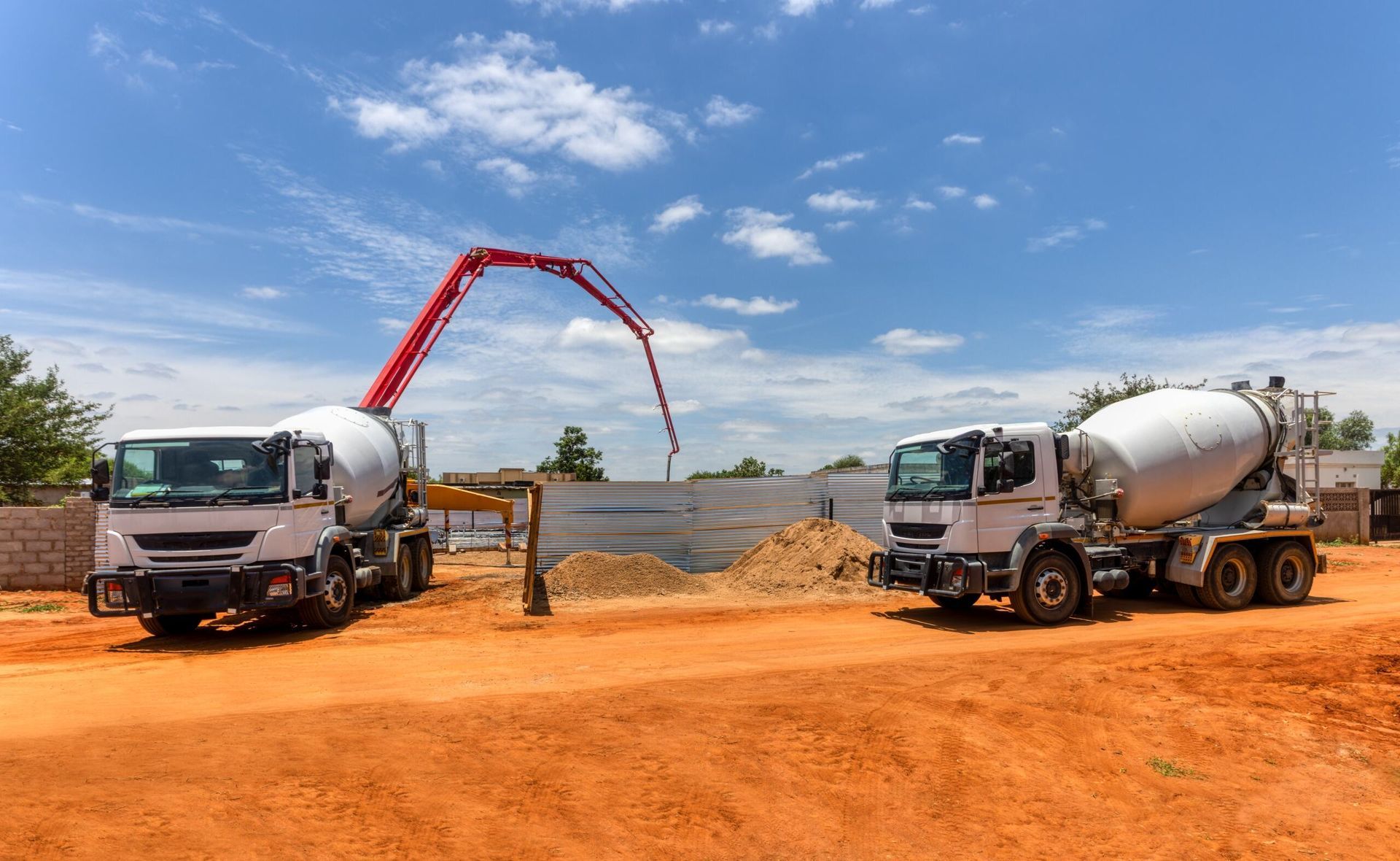 Two White Cement Trucks at A Construction Site, One with A Red Pump Arm Pouring Concrete, on Reddish Dirt Under a Blue Sky — Zappala Quarries in Gordonvale, QLD
