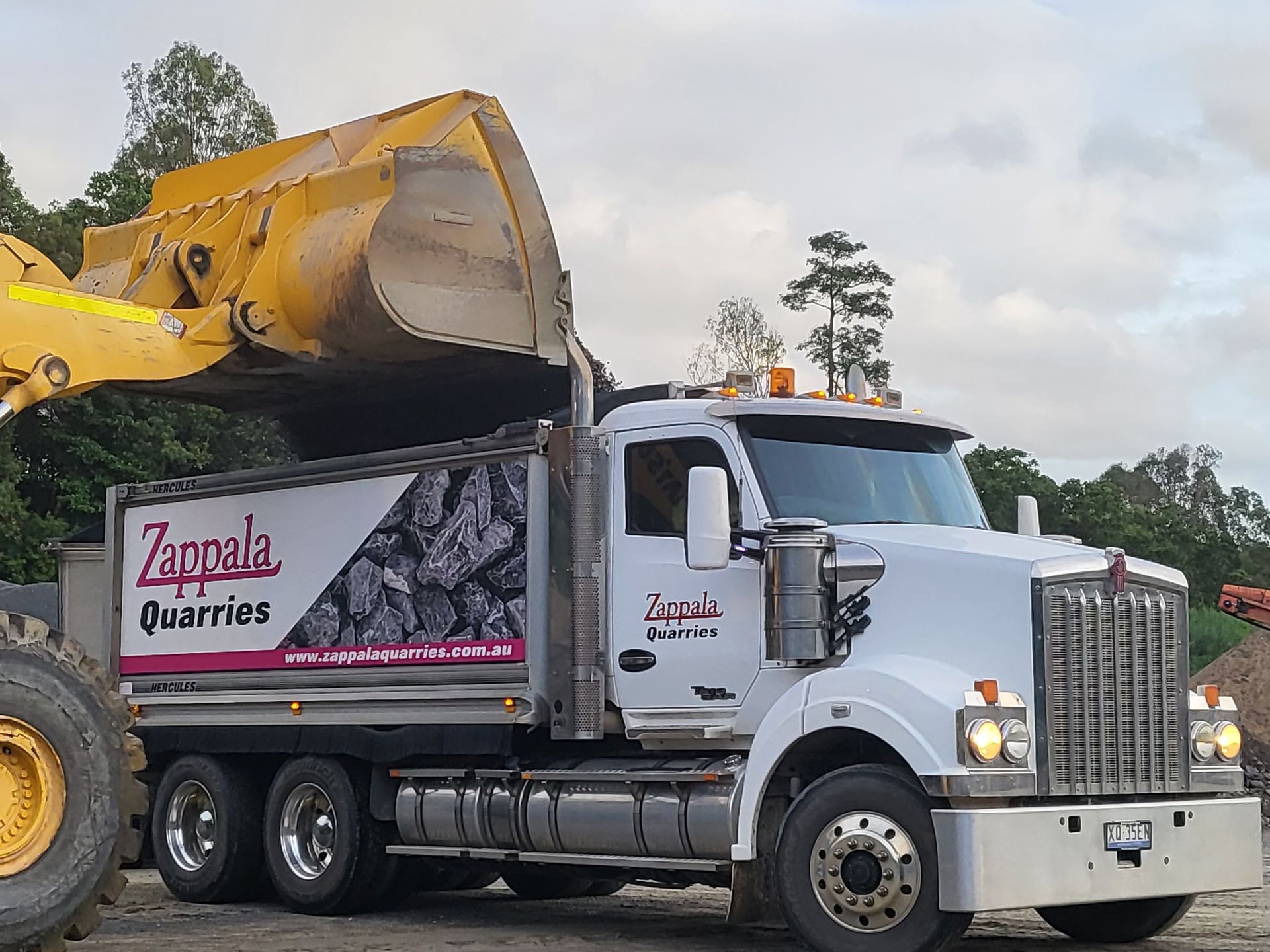 A white Zappala Quarries truck being loaded with material by a yellow excavator — Zappala Quarries in Gordonvale, QLD