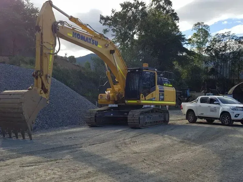A Yellow Excavator Is Parked Next to A White Truck in A Gravel Lot — Zappala Quarries in Gordonvale, QLD