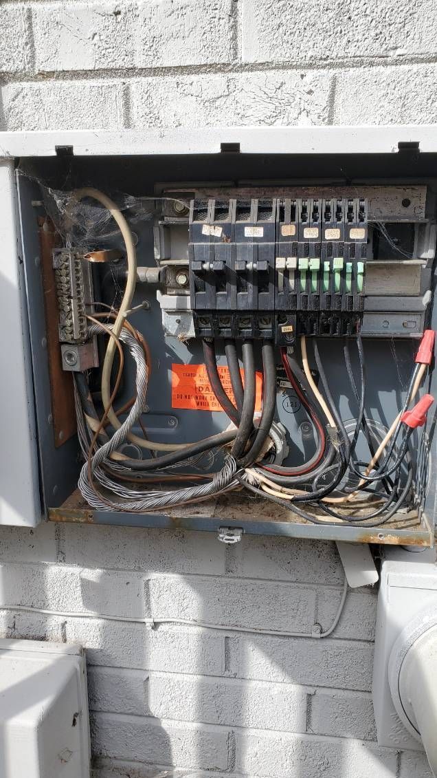 Open outdoor electrical panel with various wires and breakers.