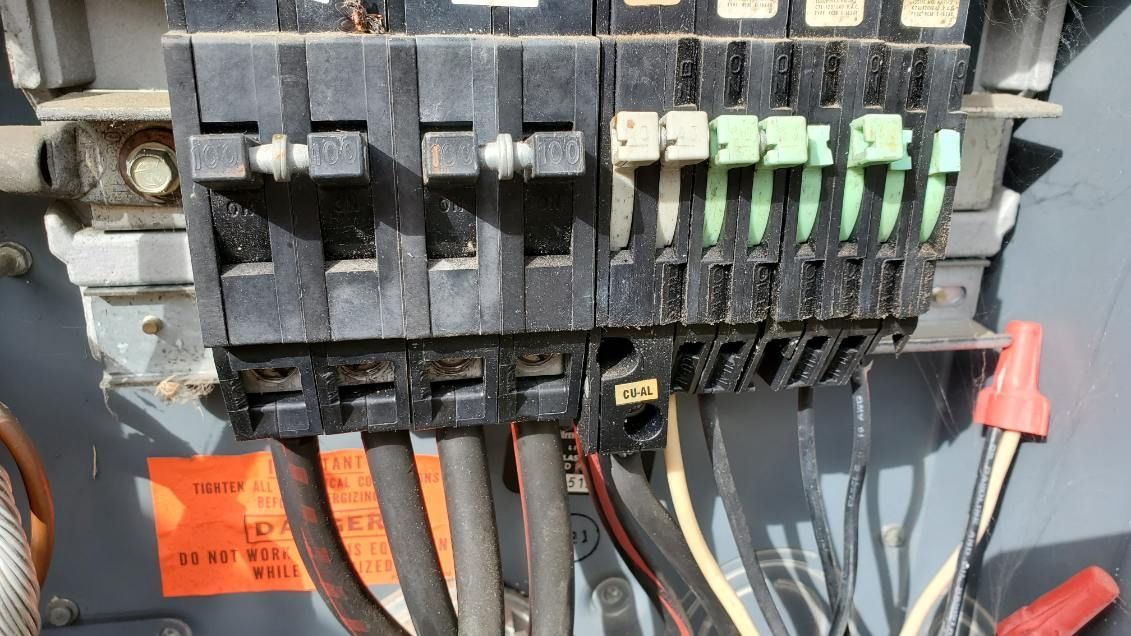 Circuit breaker panel with black and green breakers; wires attached.