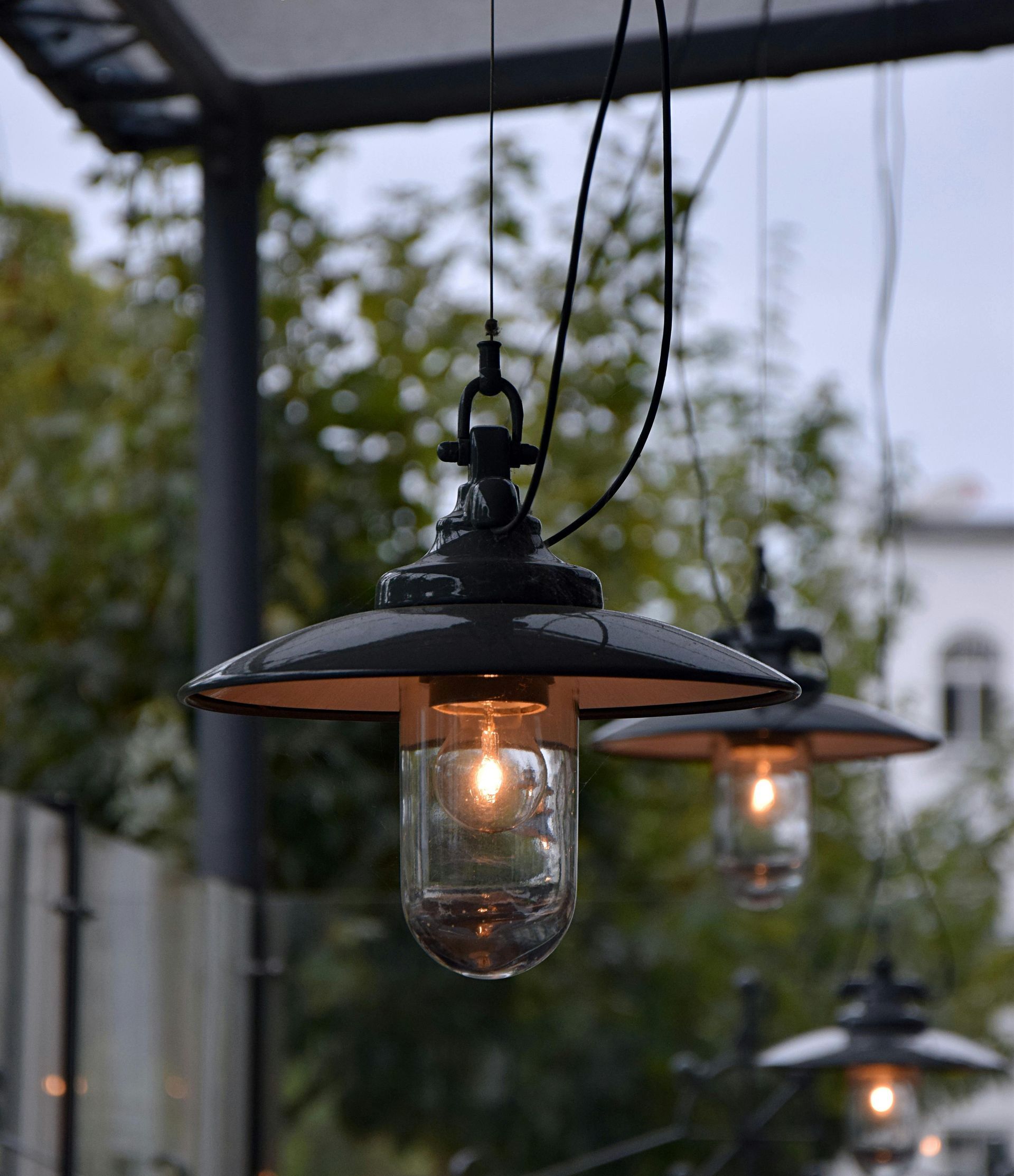 Hanging outdoor lights with black shades and clear glass, illuminating a patio area.