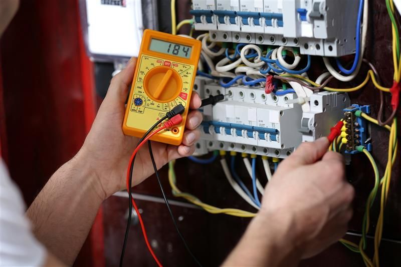 Electrician using a multimeter to test a circuit board, measuring 184 volts.
