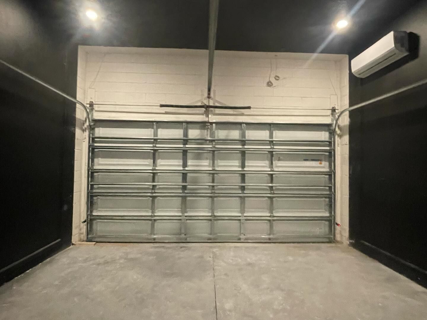 An empty garage with a garage door open and a fan on the wall.